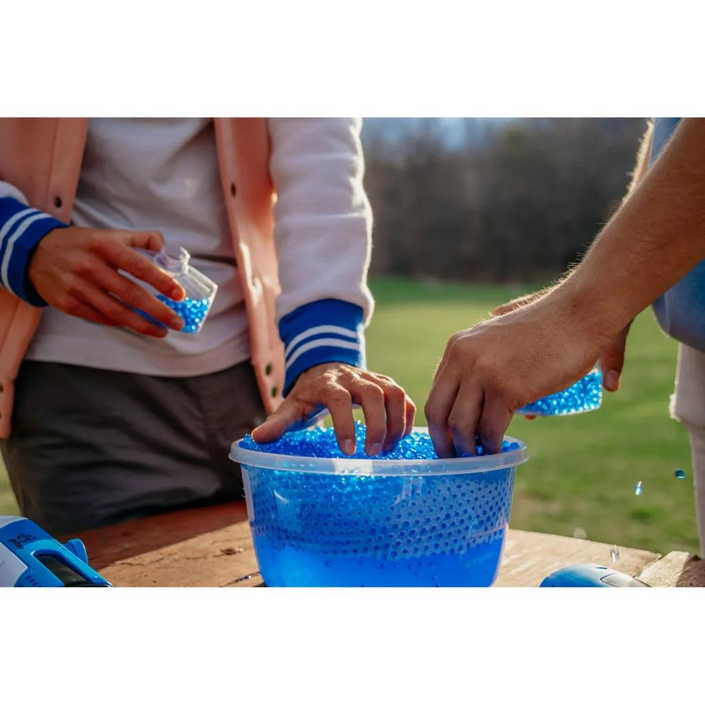 Preparing water beads for Gelbee blaster action. Two people are shown with a large tub of blue water beads, essential for refilling Gelbee gel-BB blasters for continuous fun.