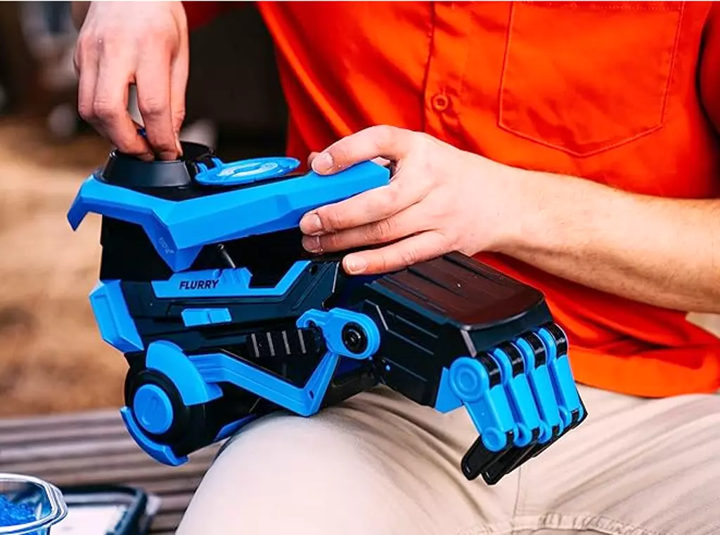 Close-up of the Gelbee Flurry Glove Water Bead Gel-BB Blaster in blue, worn on a person's hand, ready for outdoor gel blaster fun. Features an ergonomic design for active play and exciting water bead battles